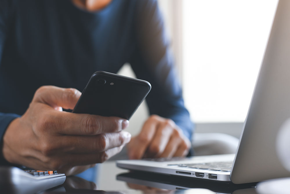 man-looking-at-phone-and-laptop